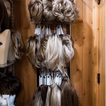 Various wigs hanging on a wooden wall in a wig shop.