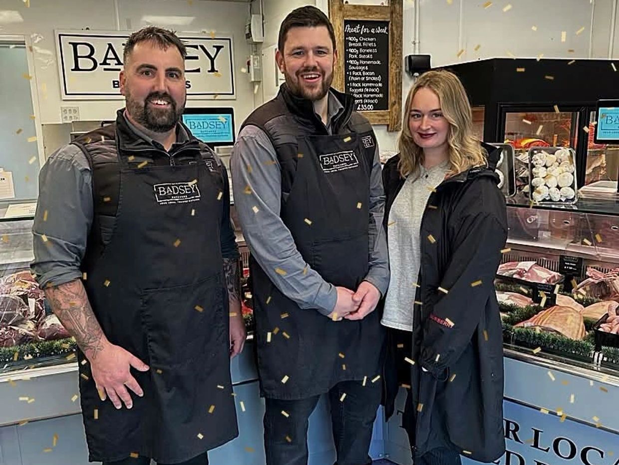 Three people standing in a butcher shop smiling.