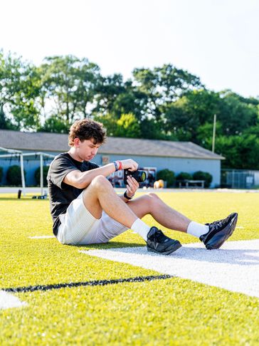 Young man sitting on a sports field, adjusting a camera.