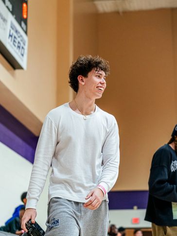 Young man smiling and holding a camera in a gymnasium.