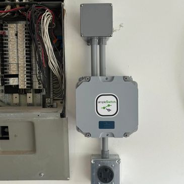 Electrical setup with a SimpleSwitch device installed next to a circuit breaker panel.
