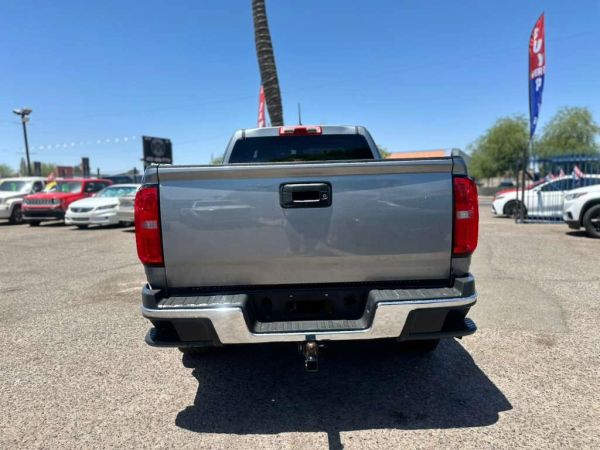 Rear view of a silver pickup truck in a parking lot under clear blue sky.