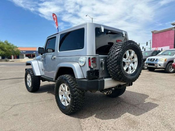 Silver off-road SUV with large tires parked in a lot under a clear sky.