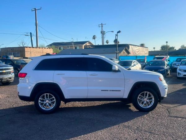 White Jeep Grand Cherokee parked in a lot under clear blue sky.