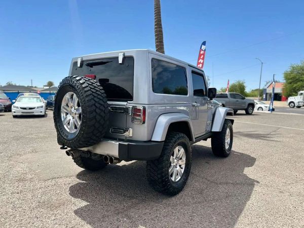 Silver Jeep Wrangler parked in a sunny lot with spare tire on back.