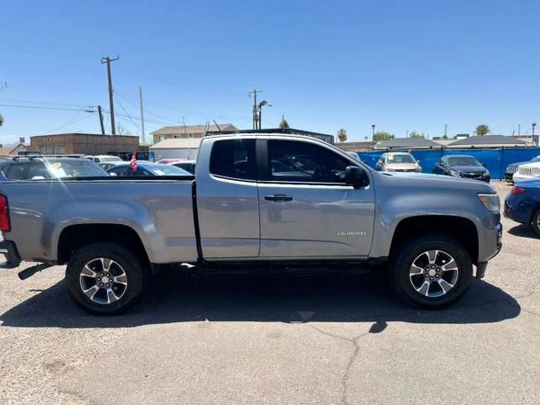 Silver Chevrolet Colorado pickup truck parked in a lot under clear blue sky.