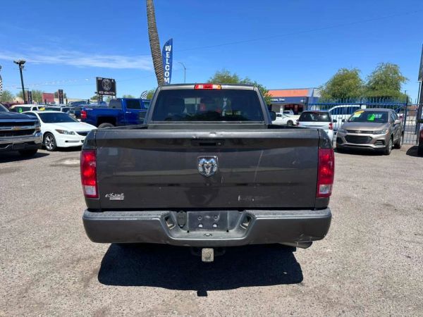 Rear view of a black Dodge Ram pickup truck in a car dealership lot on a sunny day.