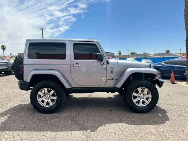 Side view of a silver Jeep Wrangler with large tires parked outdoors.