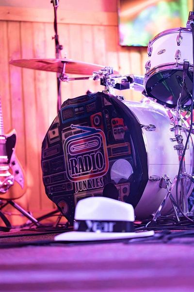 Drum set with a bass drum featuring a Radio Junkies logo and a white hat in the foreground.