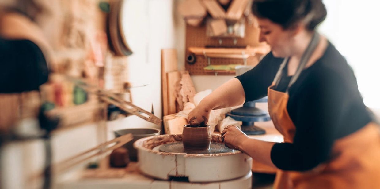 A woman shaping clay on a pottery wheel in a workshop.