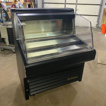 Empty refrigerated display case in a garage or workshop.