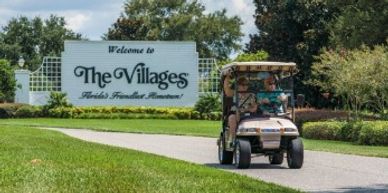 Golf cart driving near The Villages entrance sign.