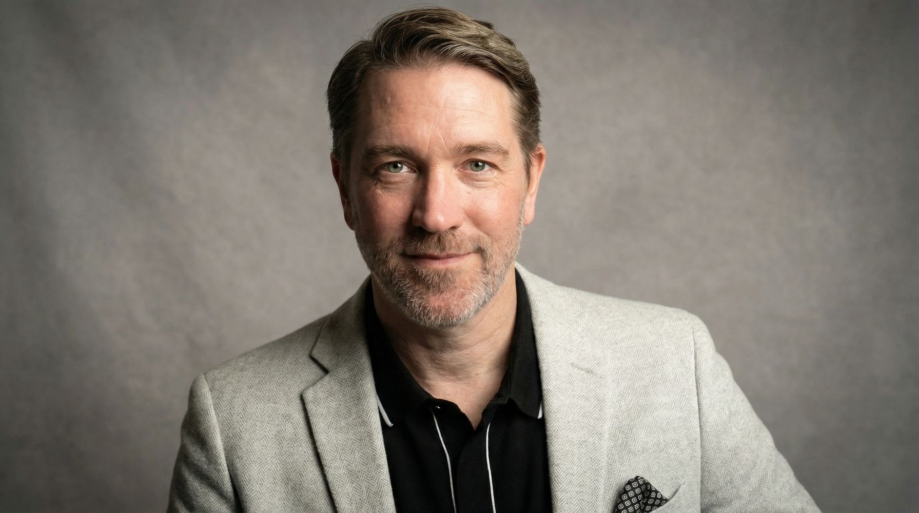 Studio picture of author posed with a calm smile, warm lighting and a soft grey backdrop.