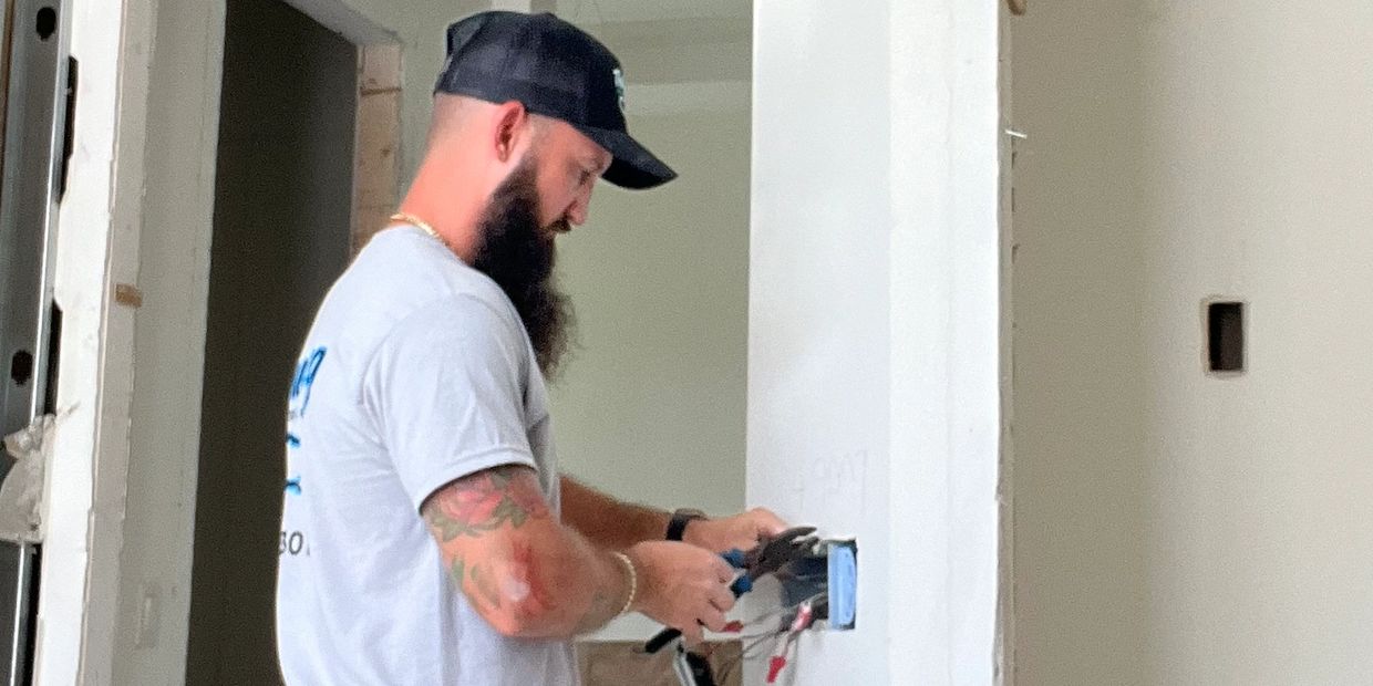 Man working on electrical wiring in a white room.