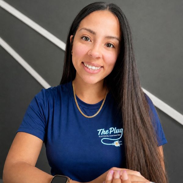 Smiling woman in blue 'The Plug' t-shirt with long hair.