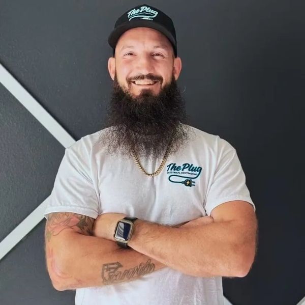 Smiling man with a beard wearing a The Plug cap and t-shirt.