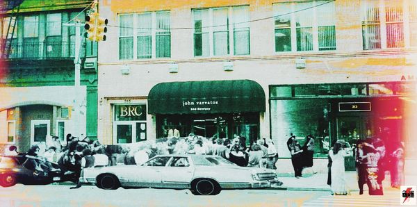 Crowded street scene in front of John Varvatos store with vintage car and people.