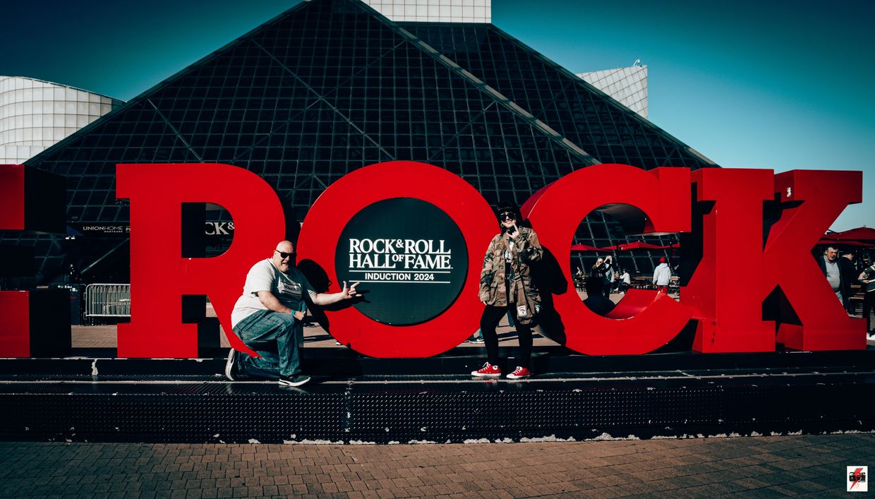 Two people posing with the large red ROCK sign at the Rock &amp; Roll Hall of Fame 2024 induction.