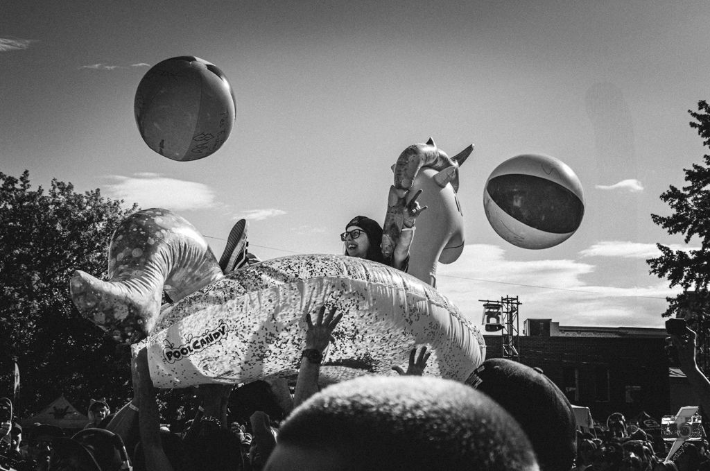 Person crowd surfing on an inflatable unicorn at an outdoor event with beach balls.