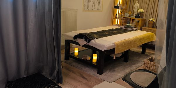 Gemütlicher Behandlungsraum mit Massagebank und Kerzenlicht.