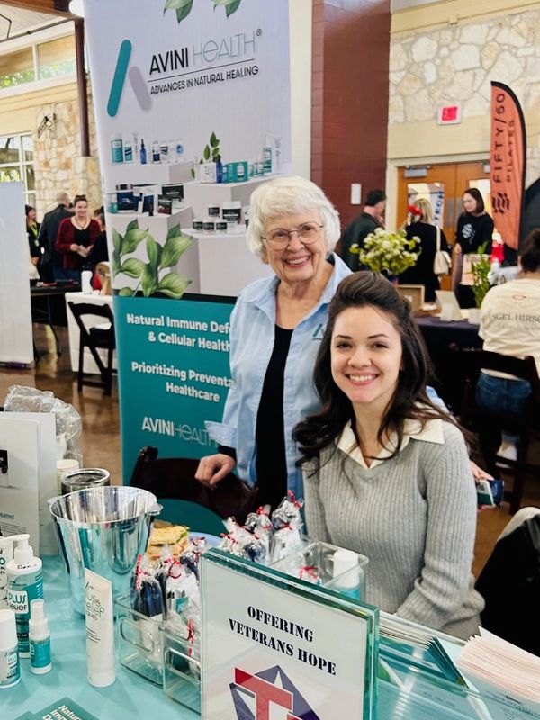 Two women smiling at a health booth offering veterans hope and natural healing products.