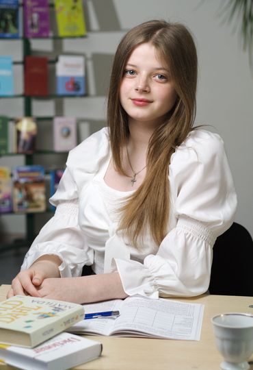 Young woman with long hair sitting at a table with books and papers.