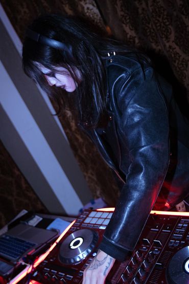 DJ with headphones mixing on a controller in a dark room.