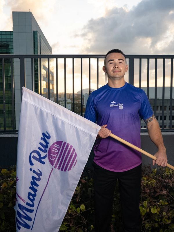 Man holding a Miami Run Club flag on a rooftop at sunset.