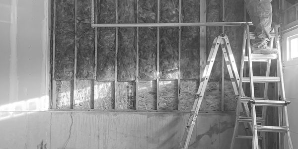A worker installs insulation in a garage wall using a ladder.