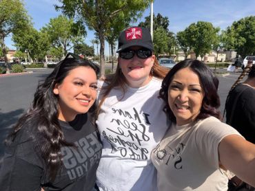 Three women smiling outdoors on a sunny day.