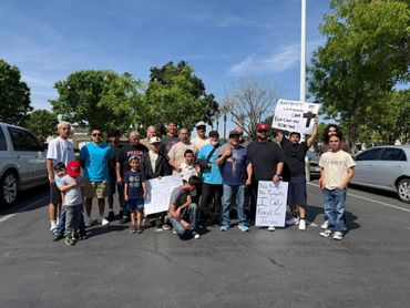 Group of people holding signs and standing together outdoors in a parking lot.