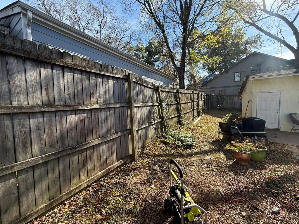 Leaning wooden fence along a backyard on a sunny day.