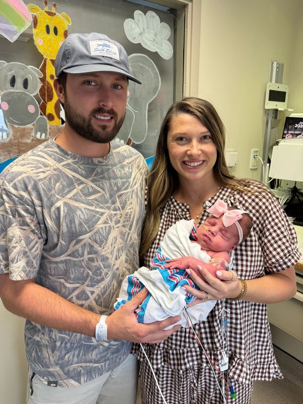 Parents smiling while holding newborn baby in hospital.