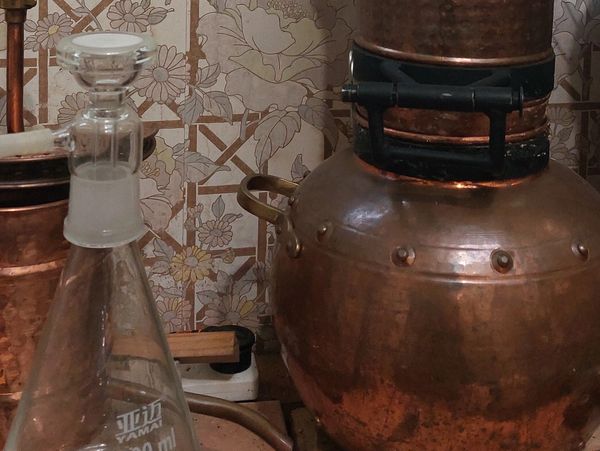 Copper distillation apparatus in a rustic lab setting with glassware and posters.