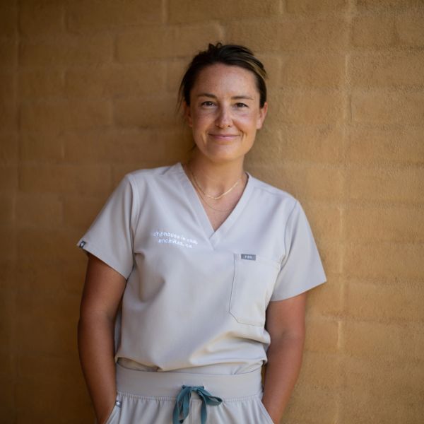 Smiling woman in beige medical scrubs standing against a tan wall.