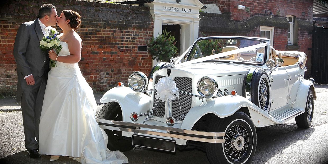 bride and groom kissing in front of vintage Beauford wedding car