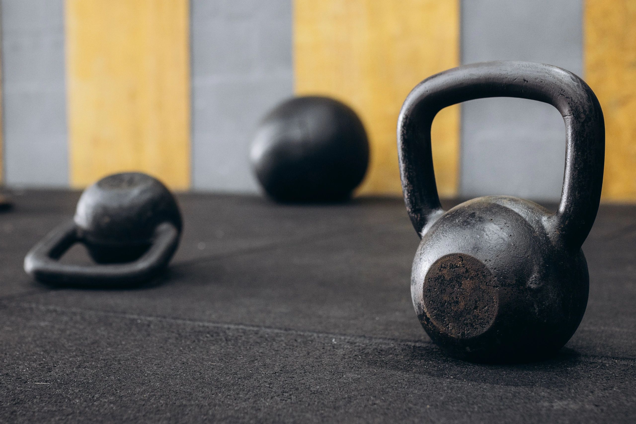 Close-up of kettlebells on a gym floor with a striped wall background.