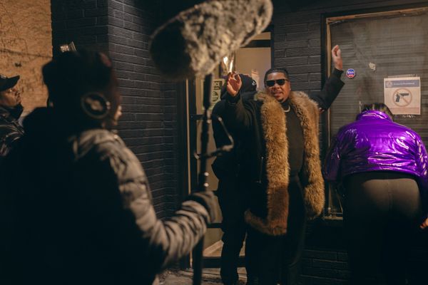 Man in fur coat celebrates on a film set.