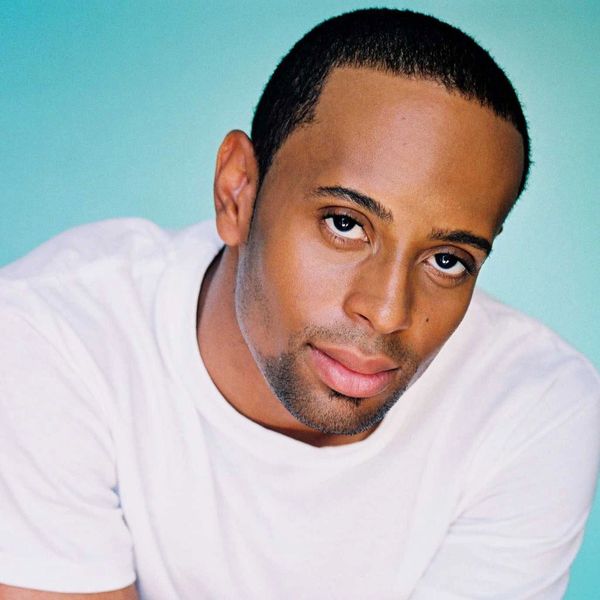 Portrait of a man with a gentle expression wearing a white shirt against a blue background.