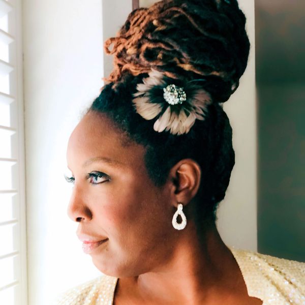 Woman with braided hair styled in a high bun, adorned with a decorative flower and wearing elegant earrings.