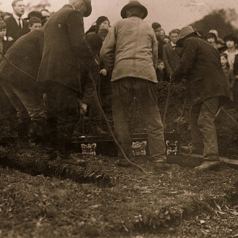 A group of people lowering a casket into its final resting place. 
