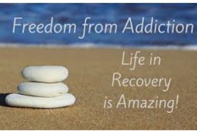 Stacked white stones on sand with text about addiction recovery.
