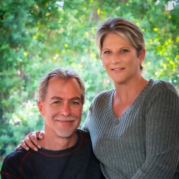 Smiling couple outdoors with greenery behind them.