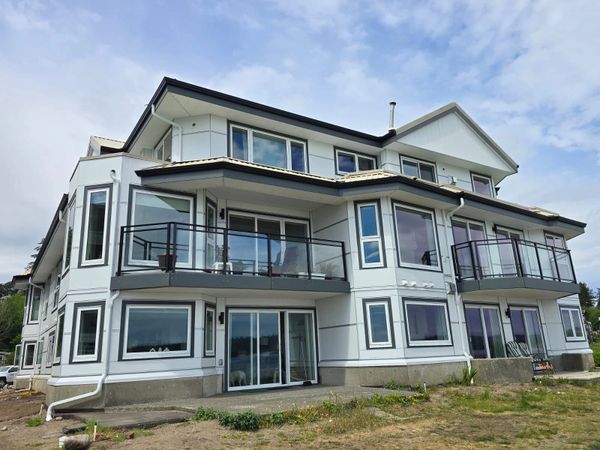 Modern multi-story house with large windows and balconies under a partly cloudy sky.