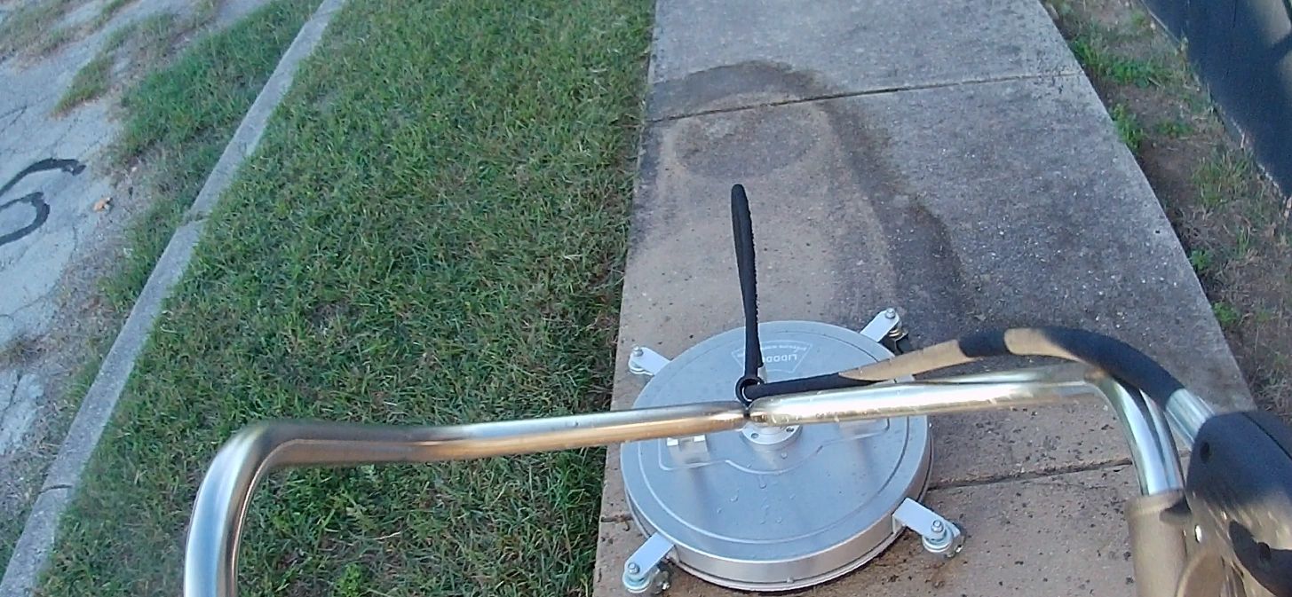 pressure washer with a surface cleaner attachment cleaning a sidewalk