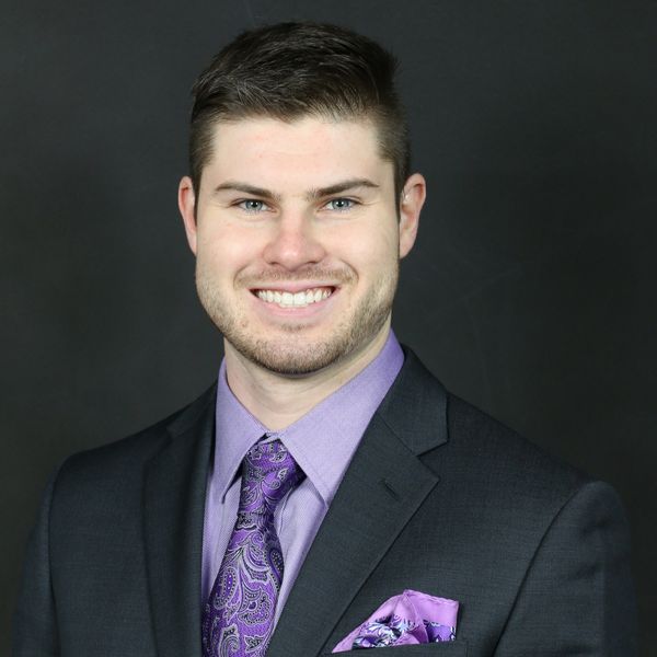 Professional headshot of a smiling man in a suit with purple tie and pocket square.
