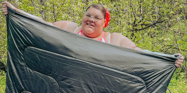 Plus Size Travel Blogger Jae Bae Productions is holding up a double size sleeping bag 