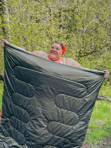 Plus Size Travel Blogger Jae Bae Productions is holding up a plus size friendly sleeping bag