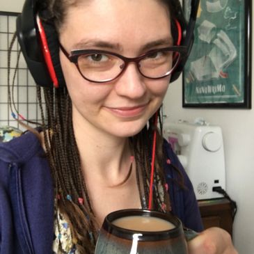 Sirah Jarocki sporting a large pair of earphones and holding up a hot mug of coffee.