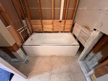 Bathtub installed in a bathroom under renovation with exposed walls and plumbing.